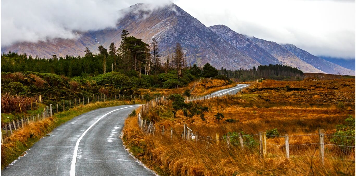 Una strada tortuosa attraversa il paesaggio del Connemara, con montagne parzialmente avvolte dalle nuvole.